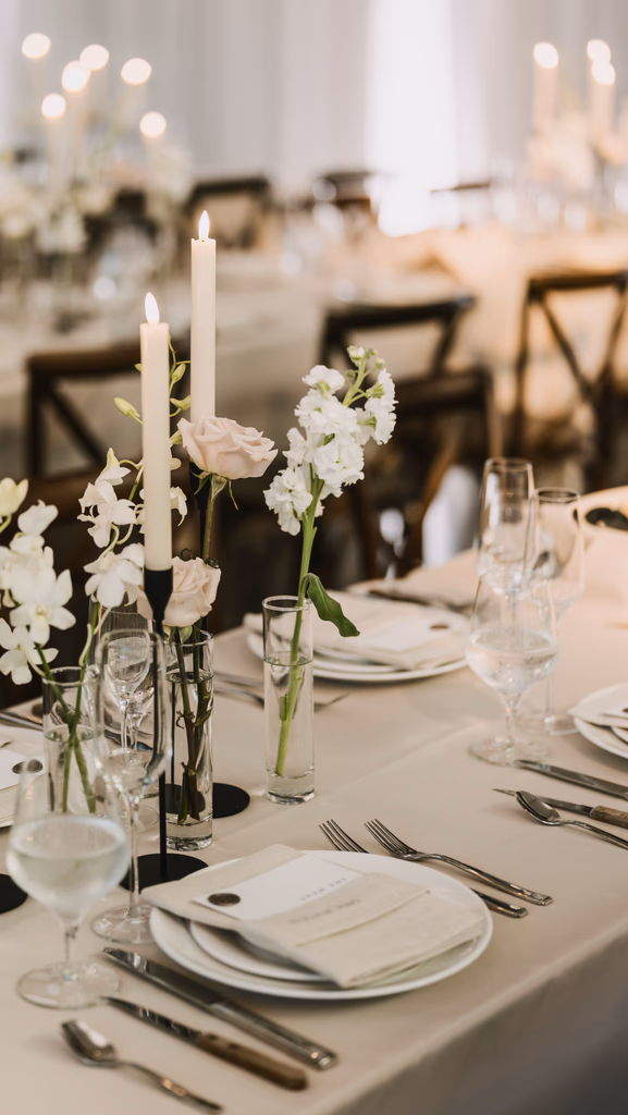Event room decorated in all white plates, candles and flowers. 